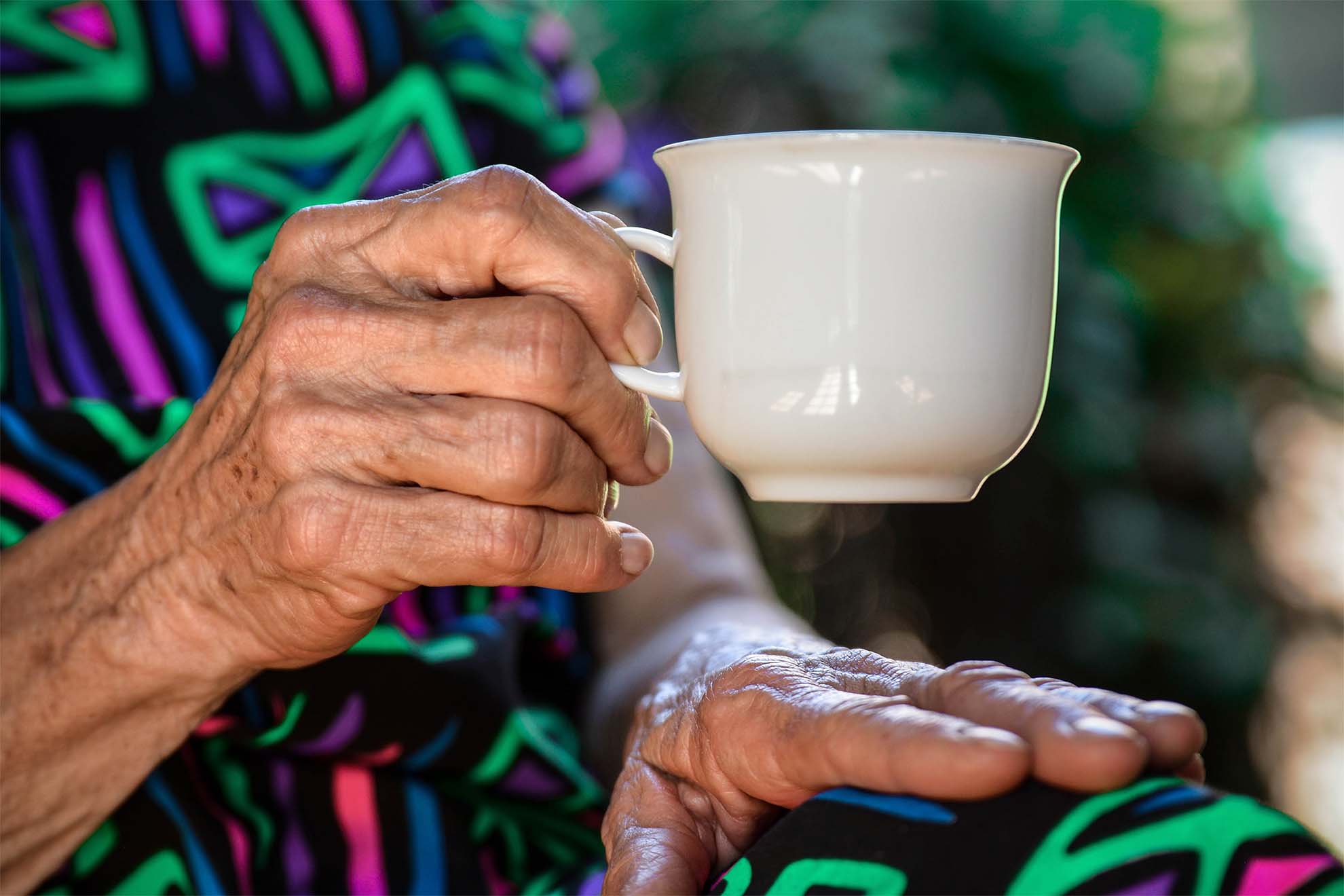 close up of an older persons hands holding a mug