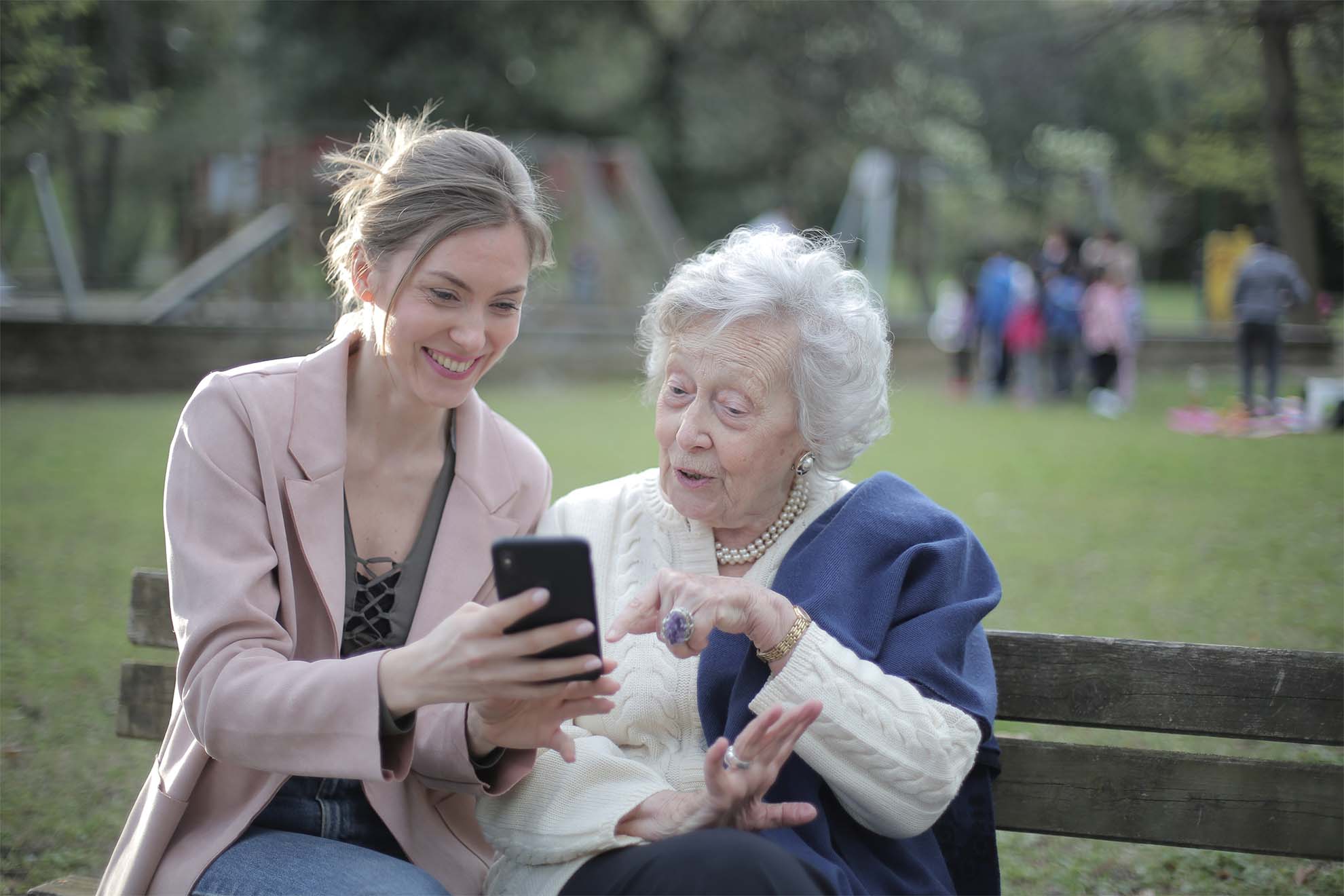 lady sat on a park bench showing her phone to an older lady